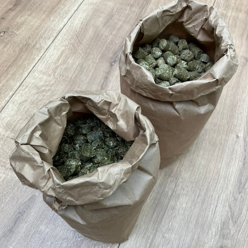 Zwei geöffnete Papiersäcke mit HEUGUT Heucobs stehen nebeneinander auf dem Hallenboden — das 5-kg- und das 25-kg-Gebinde.