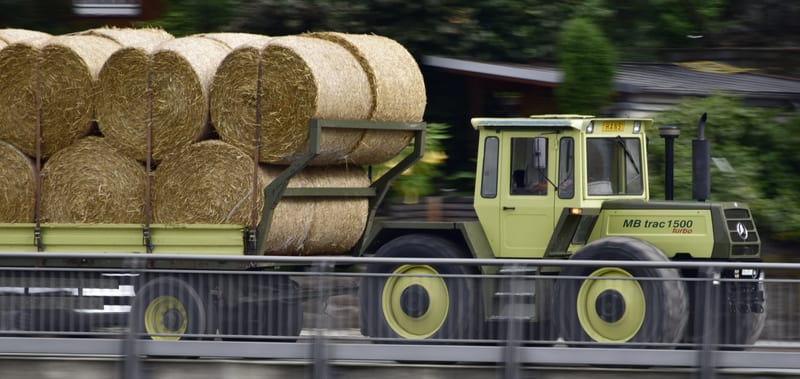 Traktor zieht einen Anhänger voller runder Heuballen vom Feld zum Hof.